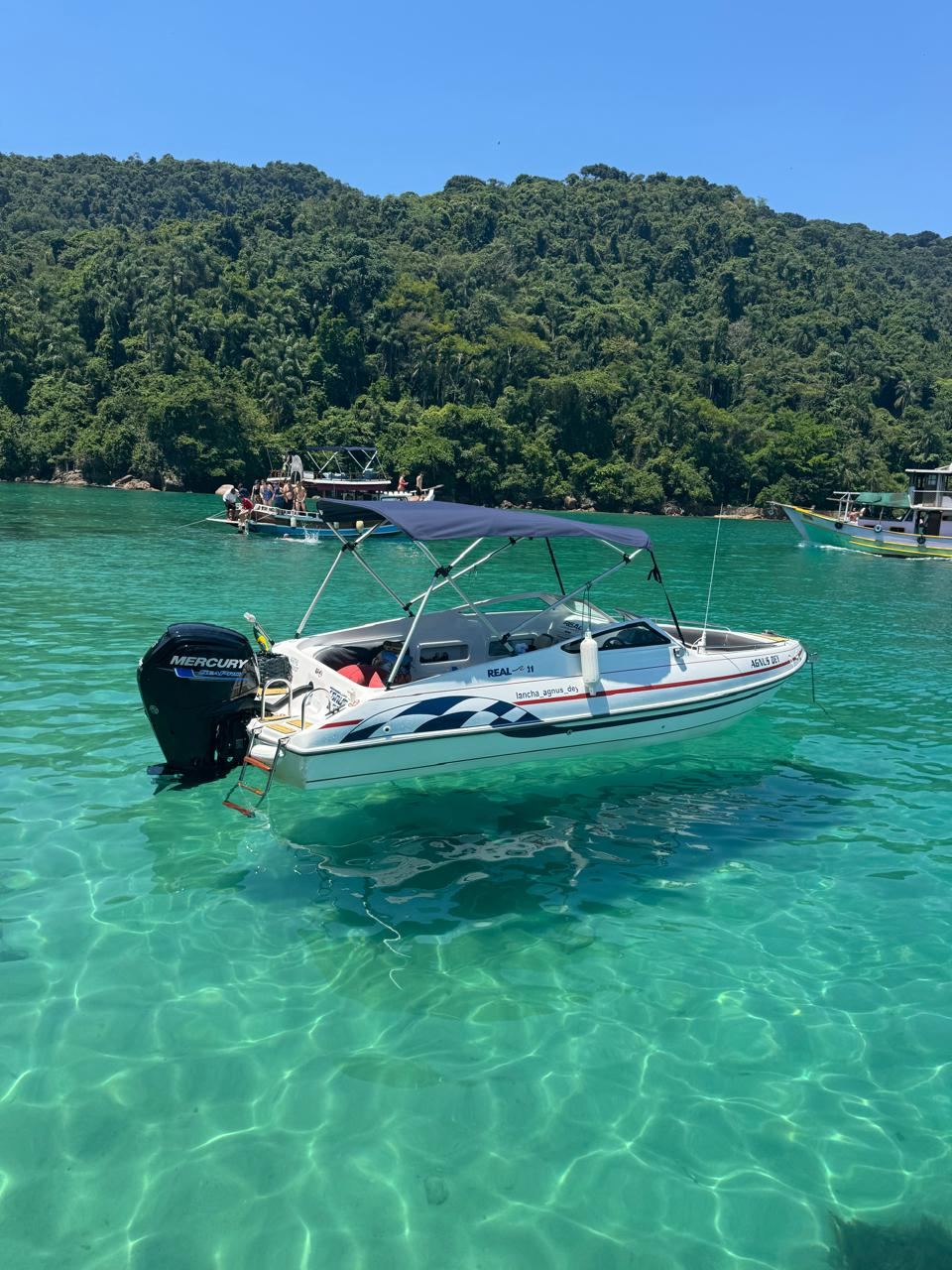 Lancha vista de lado sobre água turquesa transparente na Ilha Grande